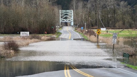 Duvall, WA, USA - March 01, 2022; Flood water covering NE 124th Street in rural King County Washington.  The Novelty Bridge is in the background as water floods in the Snoqualmie Valley.