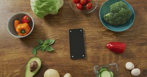 Video of healthy fruit and vegetables and smartphone on wooden background. fresh vegan food, plant based diet, healthy eating concept.