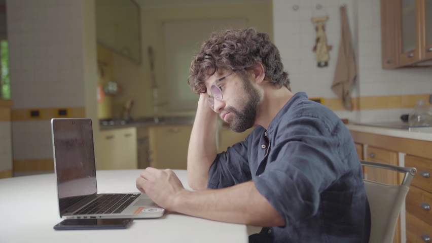 Sad anxious man with finance problem working on laptop from home worry for economy crisis, Young adult model with beard and monitor glass. Problems of depression, stress and unhappy costumer concept | Shutterstock HD Video #1088026901