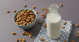 Video of fresh fruit almonds in a bowl and glass bottle of milk on grey background. fresh vegan food, plant based diet, healthy eating concept.