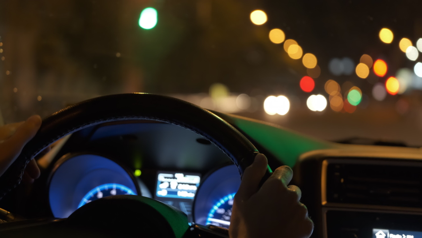 Close up of driver hands holding steering wheel driving car with blurred city street lights on background at night Royalty-Free Stock Footage #1088027637