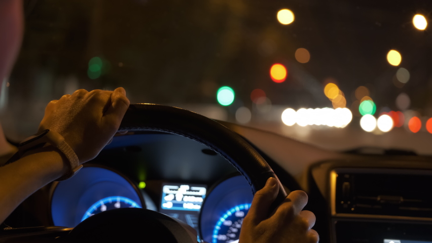 Close up of driver hands holding steering wheel driving car with blurred city street lights on background at night Royalty-Free Stock Footage #1088027637