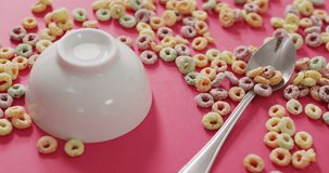Video of colorful breakfast cereals with bowl and spoon on pink background. breakfast food and cooking ingredients concept.