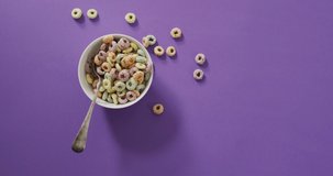 Video of colorful breakfast cereals with bowl and spoon on purple background. breakfast food and cooking ingredients concept.