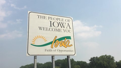 Welcome to Iowa sign pan from left to right under blue sky and bright afternoon sunlight.