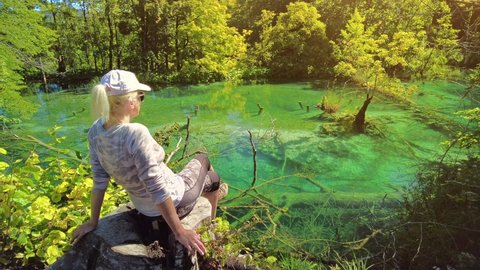 Woman sitting by the Milino Jezero lake of Plitvice Lakes National Park in Croatia, Lika region. UNESCO World Heritage of Croatia named Plitvicka Jezera.