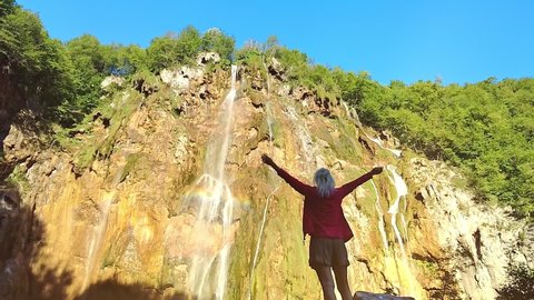 girl with open arms under the Veliki slap waterfall of Plitvice Lakes National Park in Croatia in the Lika region. UNESCO World Heritage of Croatia named Plitvicka Jezera. SLOW MOTION