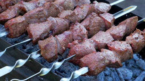 Kebab cooking outdoors on metal skewer. Traditional eastern dish - Marinated barbecue meat cooked at barbeque. Grilled pork, meat lamb, shish kebabs, shashlik. Street food, grill on charcoal and flame
