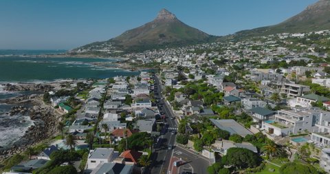 Fly above streets surrounded by residential and vacation properties. Suburb on seaside and mountain peak with steep slopes in background. Cape Town, South Africa