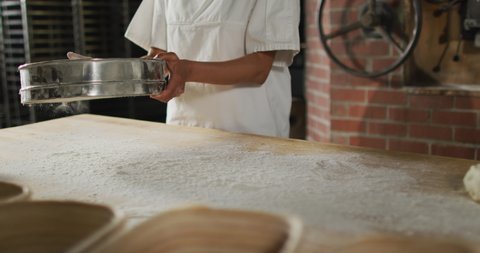 Animation of midsection of asian female baker sieving flour on board. working at bakery, independent small business.