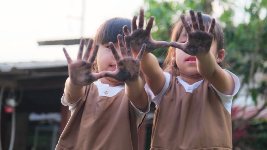 Asian sibling sisters play in the garden and show off their dirty muddy hands.