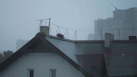 It's raining. The roof of the house. Rainy summer day. A house among new buildings. Сonstruction crane on the background