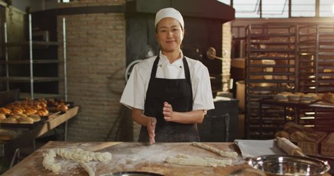 Animation of happy asian female baker cleaning hands from four and smiling at camera. working at bakery, independent small business.