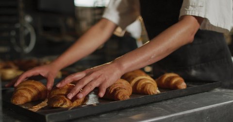 Animation of hands of asian female baker arranging croissants on tray. working at bakery, independent small business.