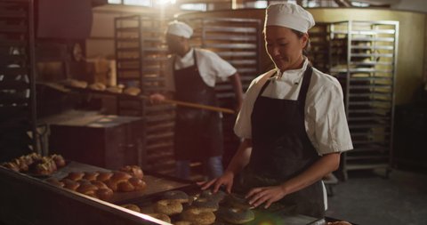 Animation of happy asian female baker arranging croissants on tray. working at bakery, independent small business.