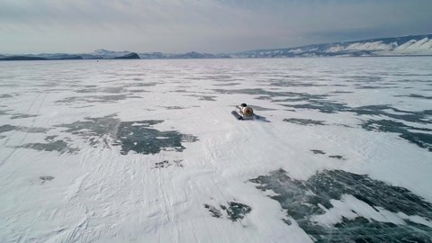 Aerial view on the hovercraft driving on cracked snowy ice of Baikal. Drone follows the vehicle. Beautiful winter landscape of lake Baikal