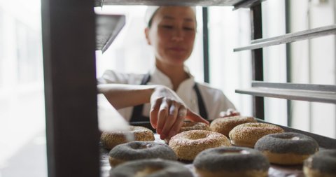 Animation of happy asian female baker checking freshly prepared doughnuts. working at bakery, independent small business.