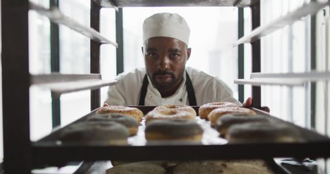 Animation of african american male baker checking freshly prepared doughnuts. working at bakery, independent small business.