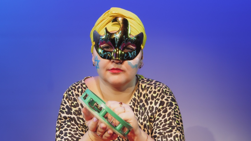 A Jewish woman in a headdress and a carnival mask commands when to make noise in the synagogue on Purim