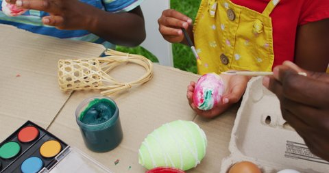 Animation of hands of diverse grandmother and grandson painting easter eggs in garden. family easter, celebration and spending quality time together outdoors.