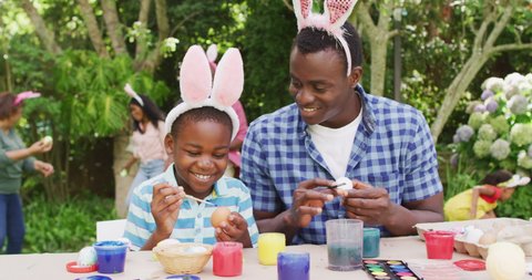 Animation of happy african american father and son painting easter eggs in garden. family easter, celebration and spending quality time together outdoors.