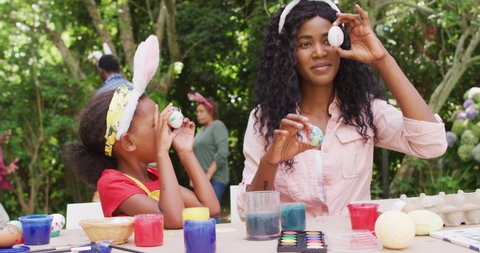 Animation of happy african american mother and daughter painting easter eggs outdoors, having fun. family easter, celebration and spending quality time together outdoors.