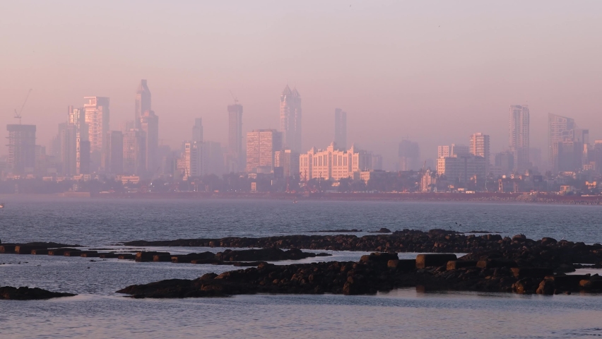 Real time wide angle view of Mumbai City Skyline as seen from famous tourist destination Marine Drive during golden hour. Wide shot of buildings during pink sunset. Bombay, Maharashtra, India.
