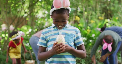 Animation of happy african american boy holding easter egg in garden. family easter, celebration and spending quality time together outdoors.