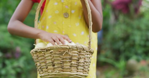 Animation of happy african american girl holding basket with easter eggs in garden. family easter, celebration and spending quality time together outdoors.
