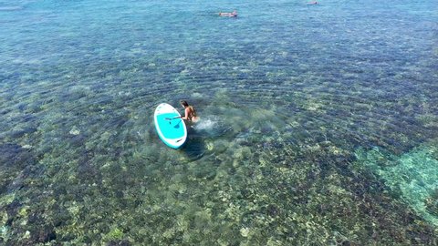 The girl walks in shallow water with a paddleboard. A woman sits on an Inflatable Stand up Paddle. Aerial view to woman on SUP board in crystal clear sea