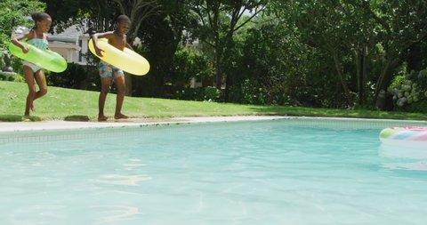 Happy african american sibling jumping into pool with inflatable wheels. family, togetherness, relax and vacations concept.