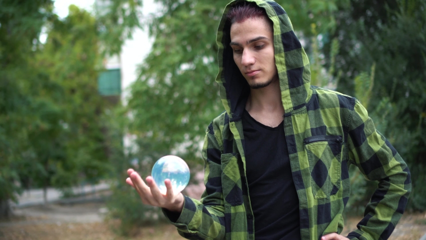 Guy shows trick with transparent glass sphere. Artist is engaged in juggling.