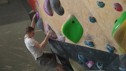 Man climber training on a climbing wall, guy practicing rock-climbing and moving up, 4k slow motion.