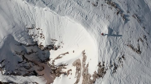 Top down drone shot of hiker walking along a snowy mountain ridge overlooking a steep drop
