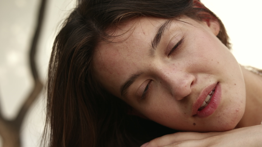 Close-up of calm caucasian young brunette woman model looking at camera on blurred white background. Girl with big blue eyes lies in her arms. Lifestyle, leisure concept, natural beauty