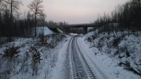 Aerial view above a Railroad and under the Bridge in Cold Forest, Winter then up to sky to Village and Hill Ridge