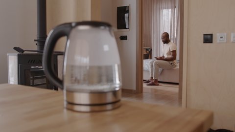 Man sitting on bed switching on water kettle with smartphone