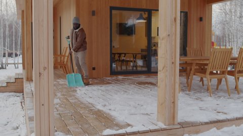 Man shovelling snow on patio of his wooden house