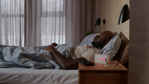 Man waking up in bed switching on light with smartphone