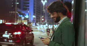 View of young man using a smartphone at night time with city view landscape in the background. Mobile phone, technology, urban concept. High quality video