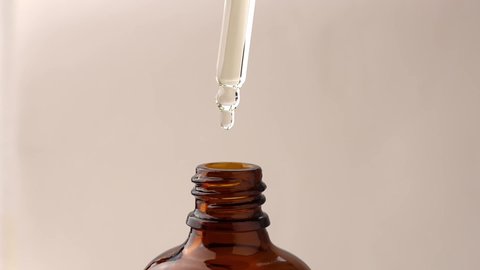 Pipette with cosmetic oil for massage and drops flowing into a brown bottle, close-up.