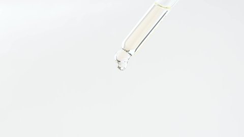 Glass dropper with cosmetic liquid on a plain background close-up.