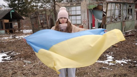 10 years old girl holding the flag of Ukraine against the background of the ruins. War in Ukraine