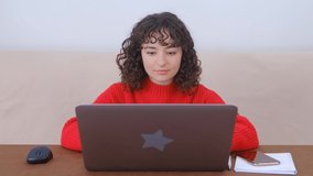 White woman studying online on laptop computer. Focused young adult female with curly hair working on modern notebook pc at home during lockdown. 4k stock video of freelancer person doing distant work