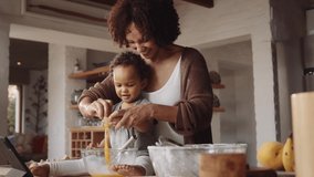 Biracial mother and daughter baking together in modern-styled kitchen. Child whisking eggs in bowl on counter, while mother kisses her on cheek. - Powered by Shutterstock - Get 15% off with code: PIKWIZARD15