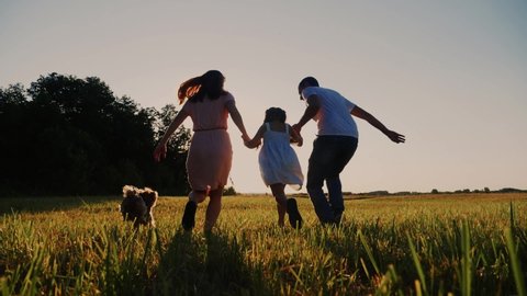 happy family running in the park. dad and mom silhouette throw up their daughter up holding hands run next to a dog in a park in nature. friendly family outdoor running together at sunset back view