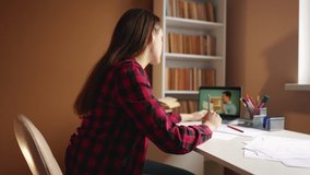 learn virtual. a teenager girl is studying remotely from a teacher online on a laptop sitting at a table next to a bookcase. distance learning education concept. student on indoor exam online