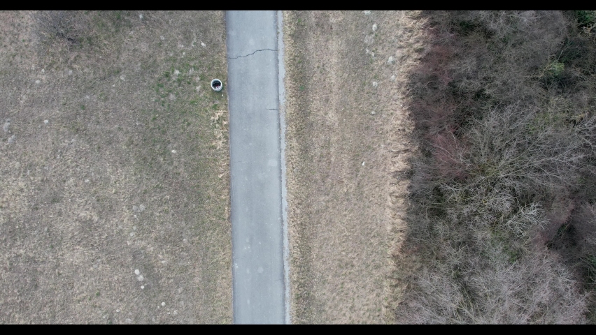 Top-down aerial drone image of the road through the forest and meadows on a winter day