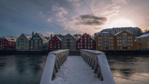 Old Town Bridge Across Nidelva River With Walkway Covered In Snow At Sunset In Trondheim, Norway. Colorful Houses In Background. time lapse