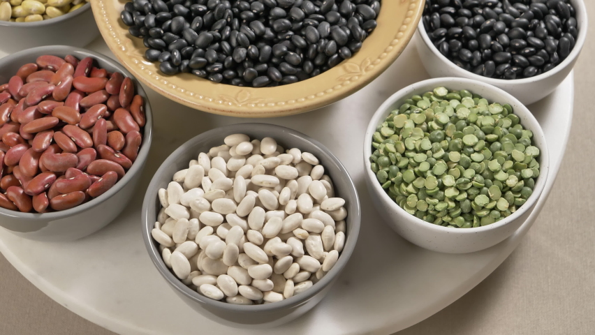 Variety beans in bowls rotating closeup. Legumes - Mayocoba, black, kidney red and white, lima beans, peas. Healthy diet, vegan protein source, plant-based food concept. Royalty-Free Stock Footage #1088064381